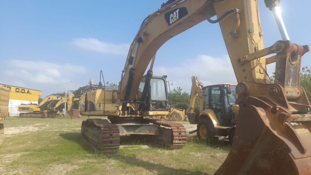 Excavadora CAT amarilla de maquinaria pesada en un campo, rodeada de otras máquinas de construcción.