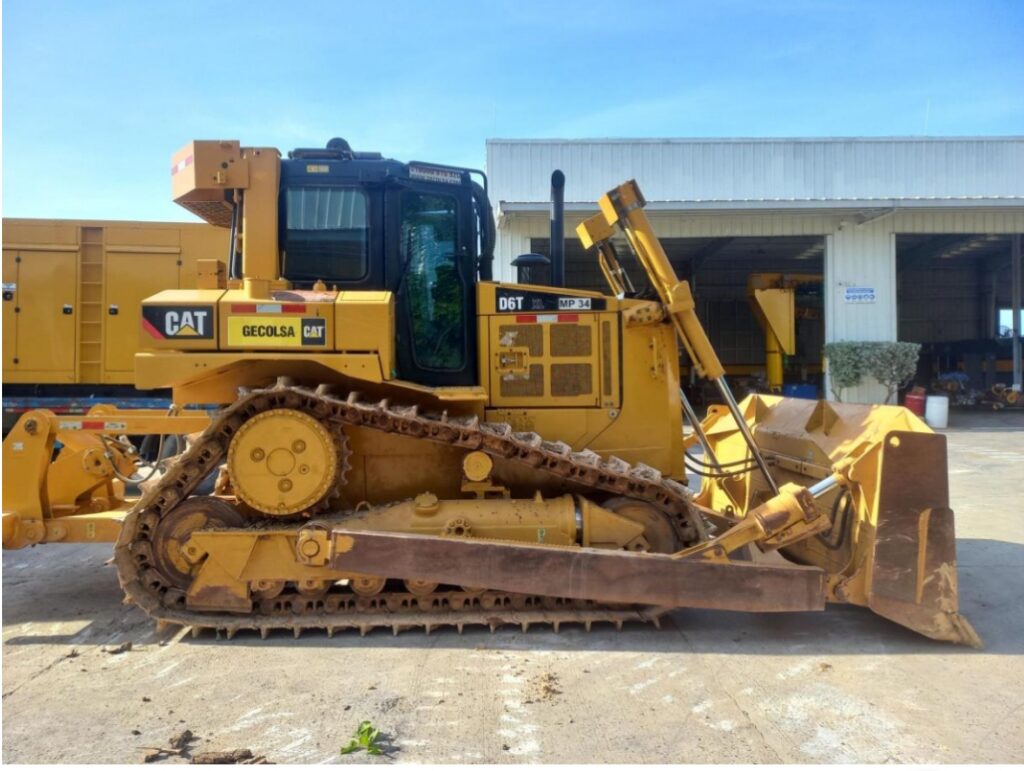 Topadora Caterpillar D6T estacionada frente a taller industrial, lista para operar en obra de construcción pesada.