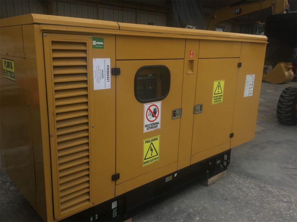 Planta eléctrica cerrada de color amarillo con señales de advertencia, en espacio industrial techado.